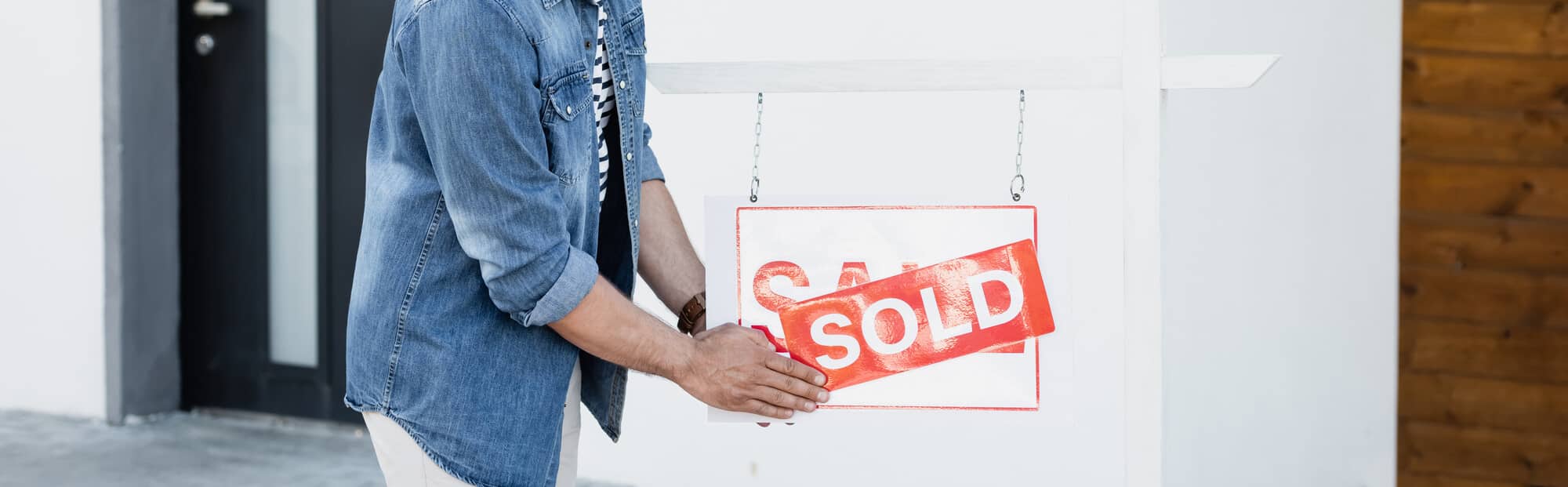 Person hanging a 'SOLD' sign on a real estate property