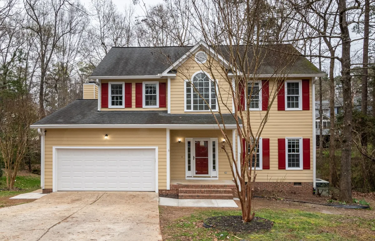 A suburban home with red shutters and surrounded by greenery.