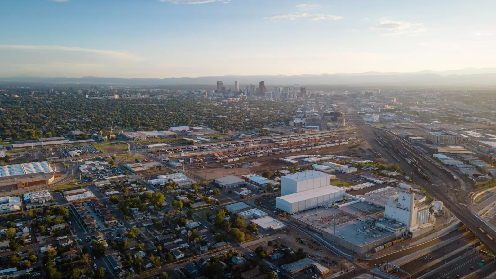 Aerial view over Denver residential neighborhoods toward the downtown skyline and the Front Range mountains at dusk
