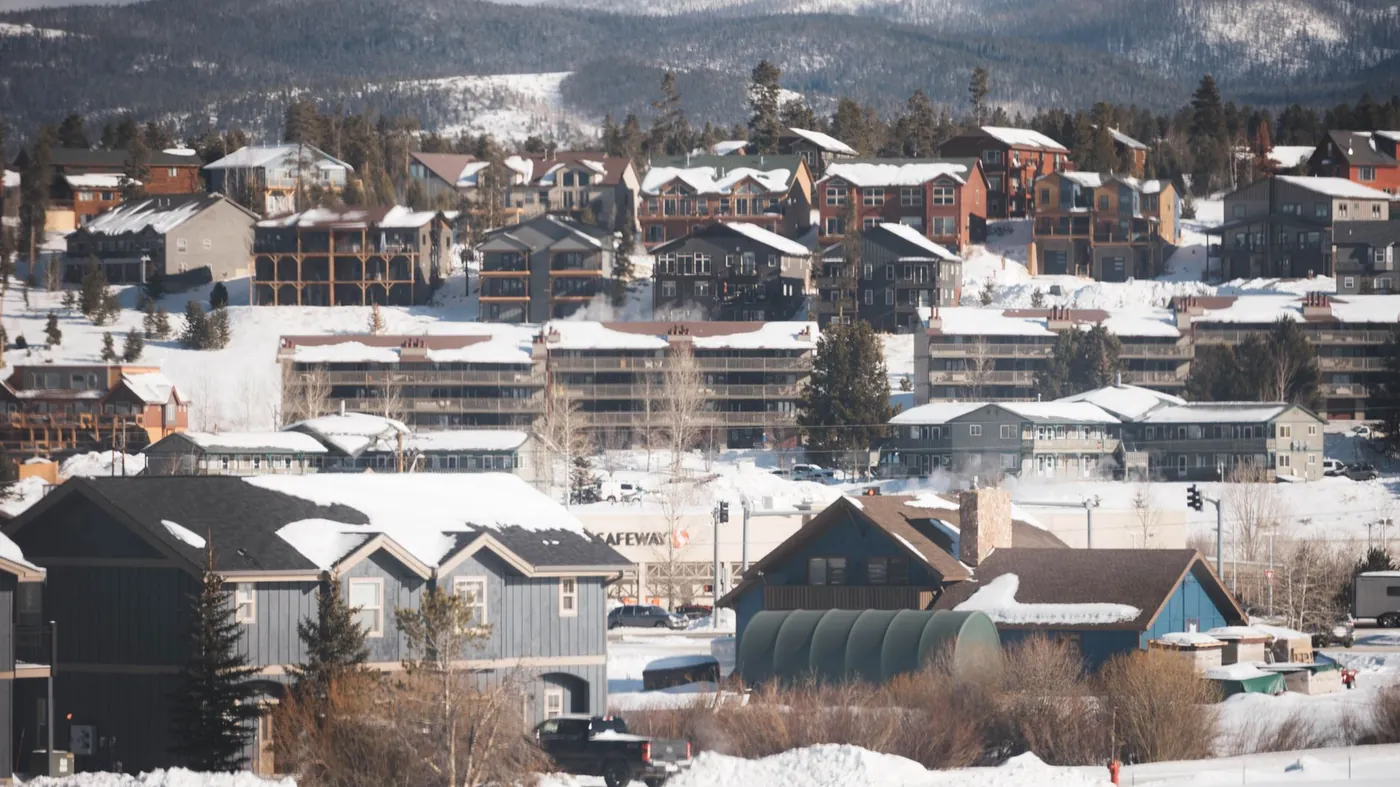 Houses and condominium buildings under deep snow in a Colorado mountain town, with forested peaks behind