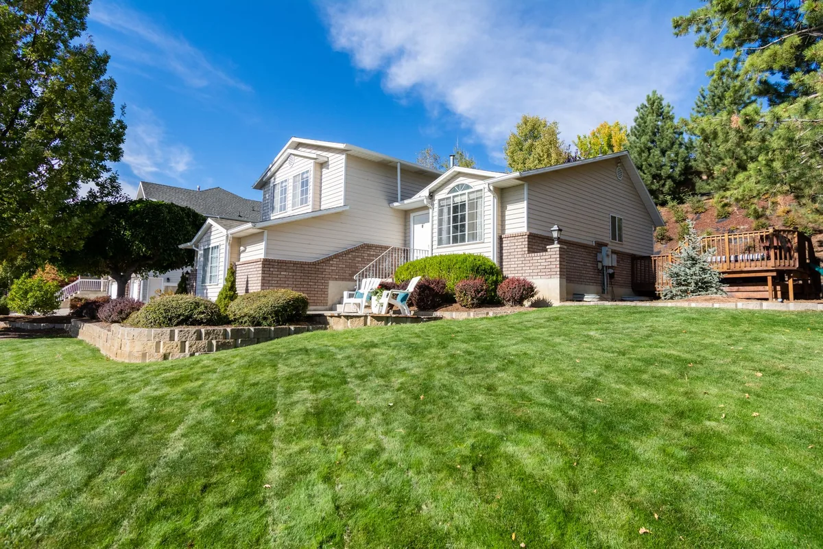 Suburban house with a manicured lawn, framed by trees and blue sky.