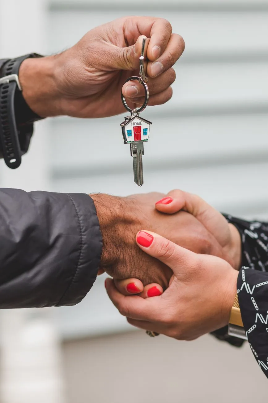 Two hands shaking while one hand holds a house-shaped key chain