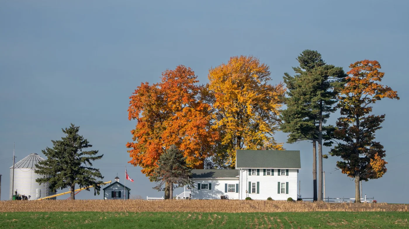 White farmhouse with a grain bin and autumn trees beside a field in Indiana