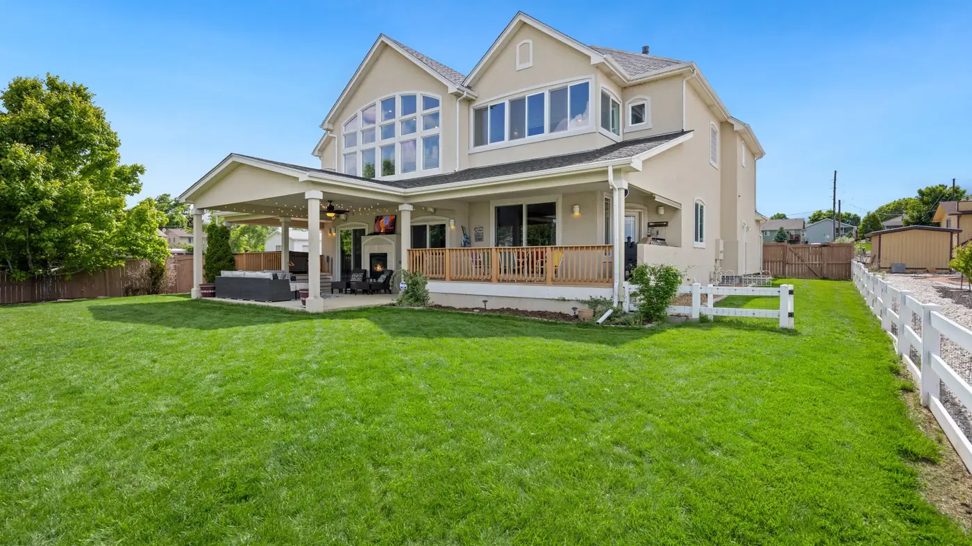 The garden side of a two-storey house, with a covered porch and deck, tall gabled windows and a wide mown lawn running to a fence