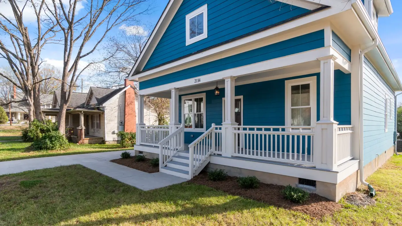 A freshly painted blue frame cottage with a deep front porch, white rails and turned posts, on a street of older houses
