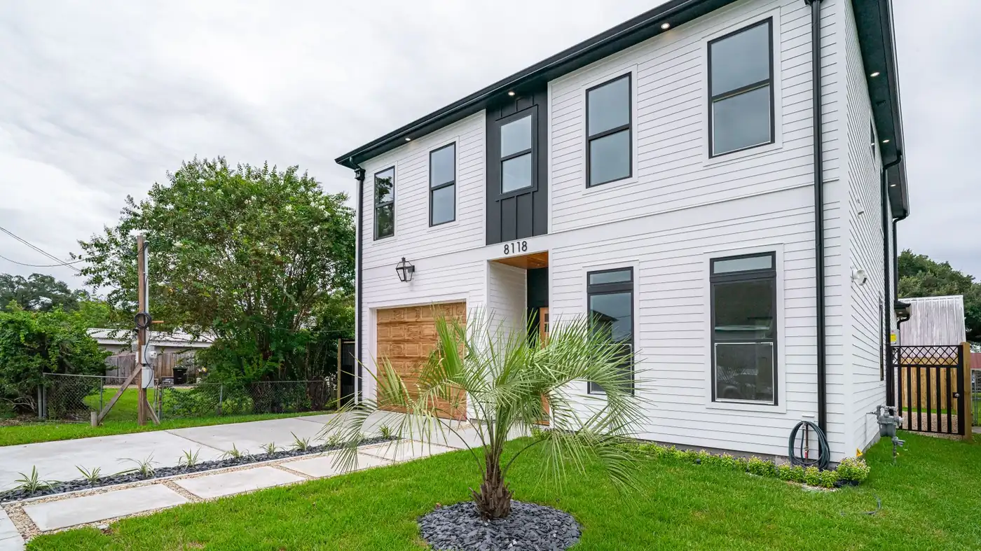 A newly built white two-storey house with a palm in the front lawn and a small palm-lined path