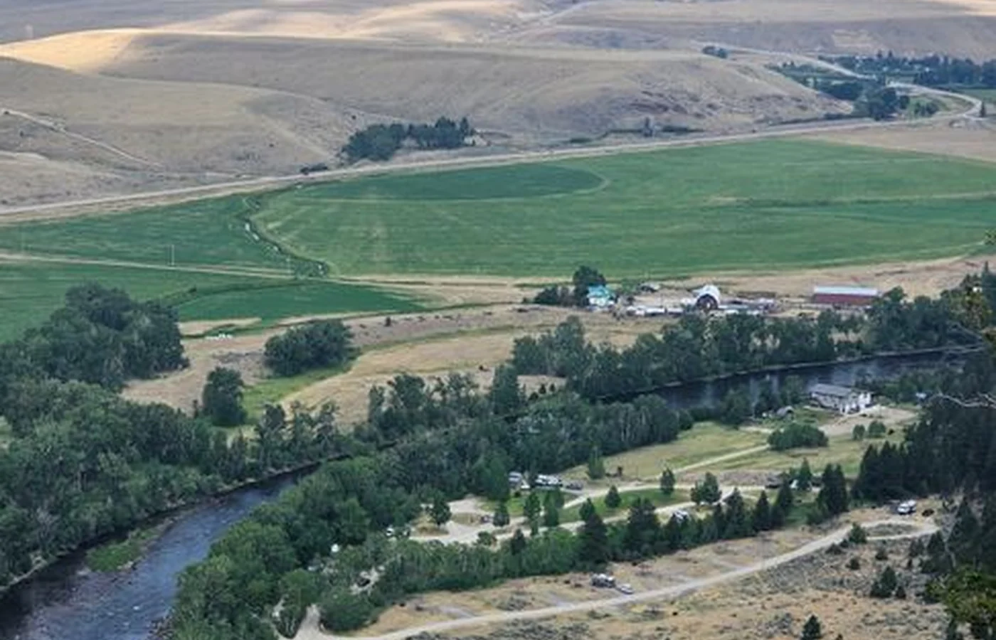An aerial view over Butte, with fields, a river and roads laid out across a broad valley and mountain ranges standing behind it
