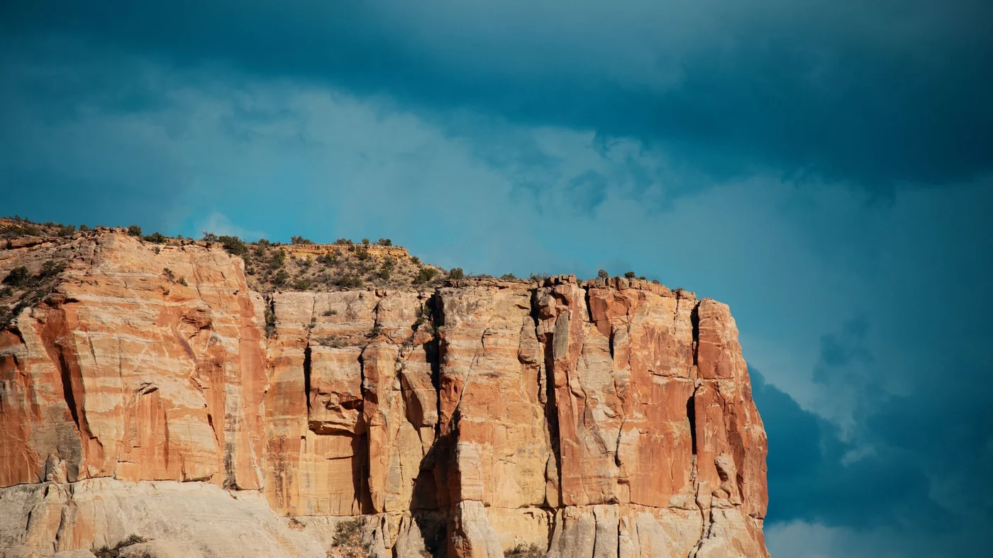 A broad flat-topped sandstone mesa rising out of high desert scrub under a deep blue sky