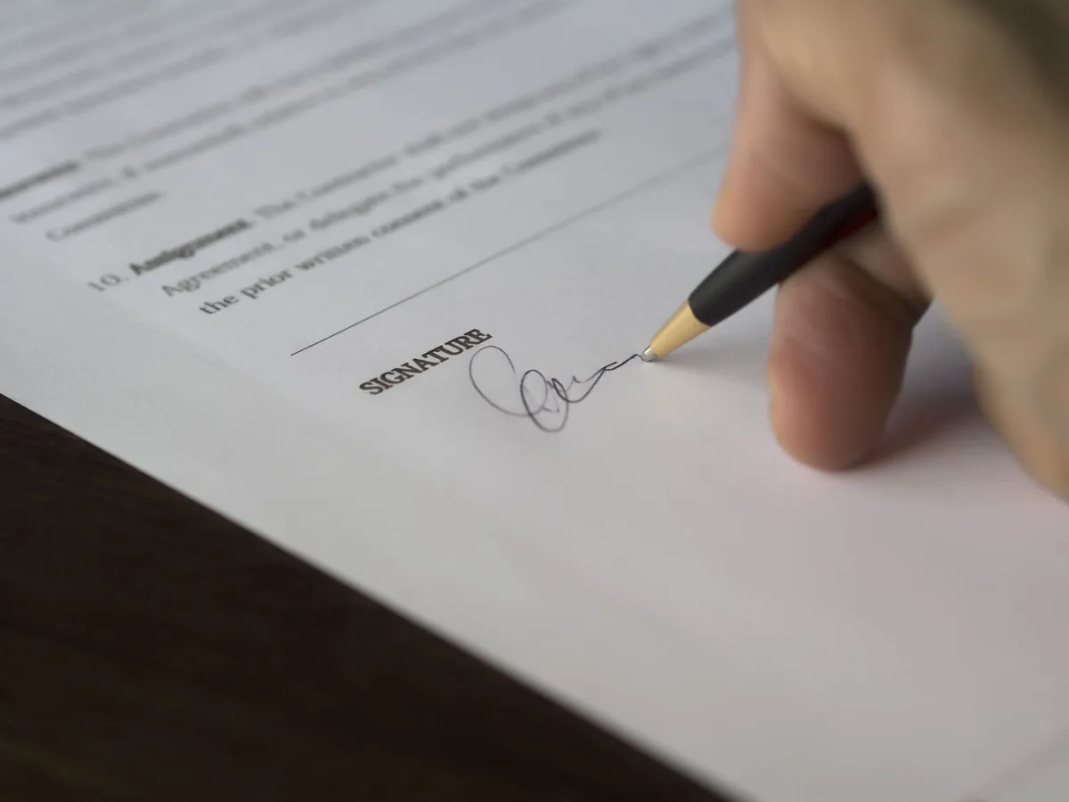 Close-up of a hand signing a contract above the signature line