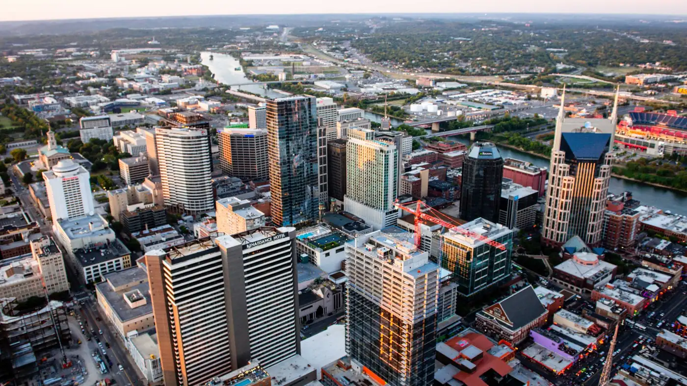 Aerial view of downtown Nashville at dusk, with the Cumberland River curving past the skyline and construction cranes over the city