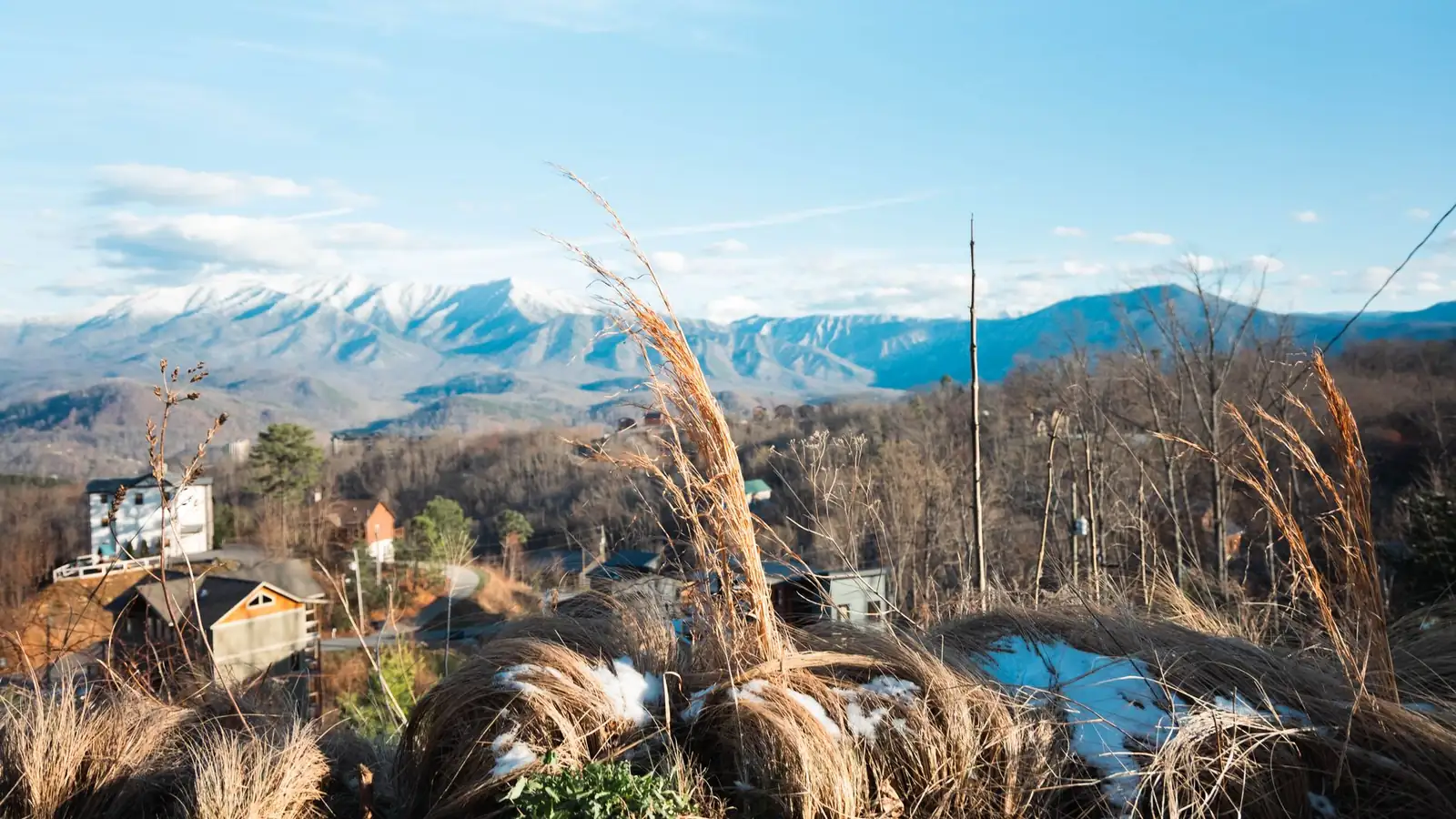 Cabins and hillside homes on a wooded ridge in east Tennessee, with the snow-dusted peaks of the Great Smoky Mountains behind