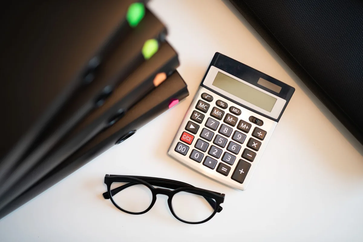 Calculator, reading glasses and stacked folders on a white desk