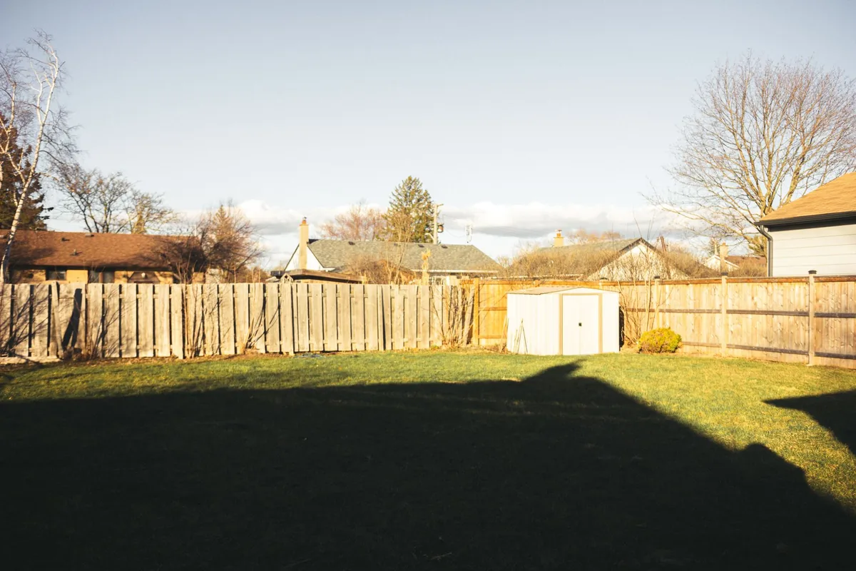 Fenced residential backyard with a lawn and a small storage shed under a clear sky.