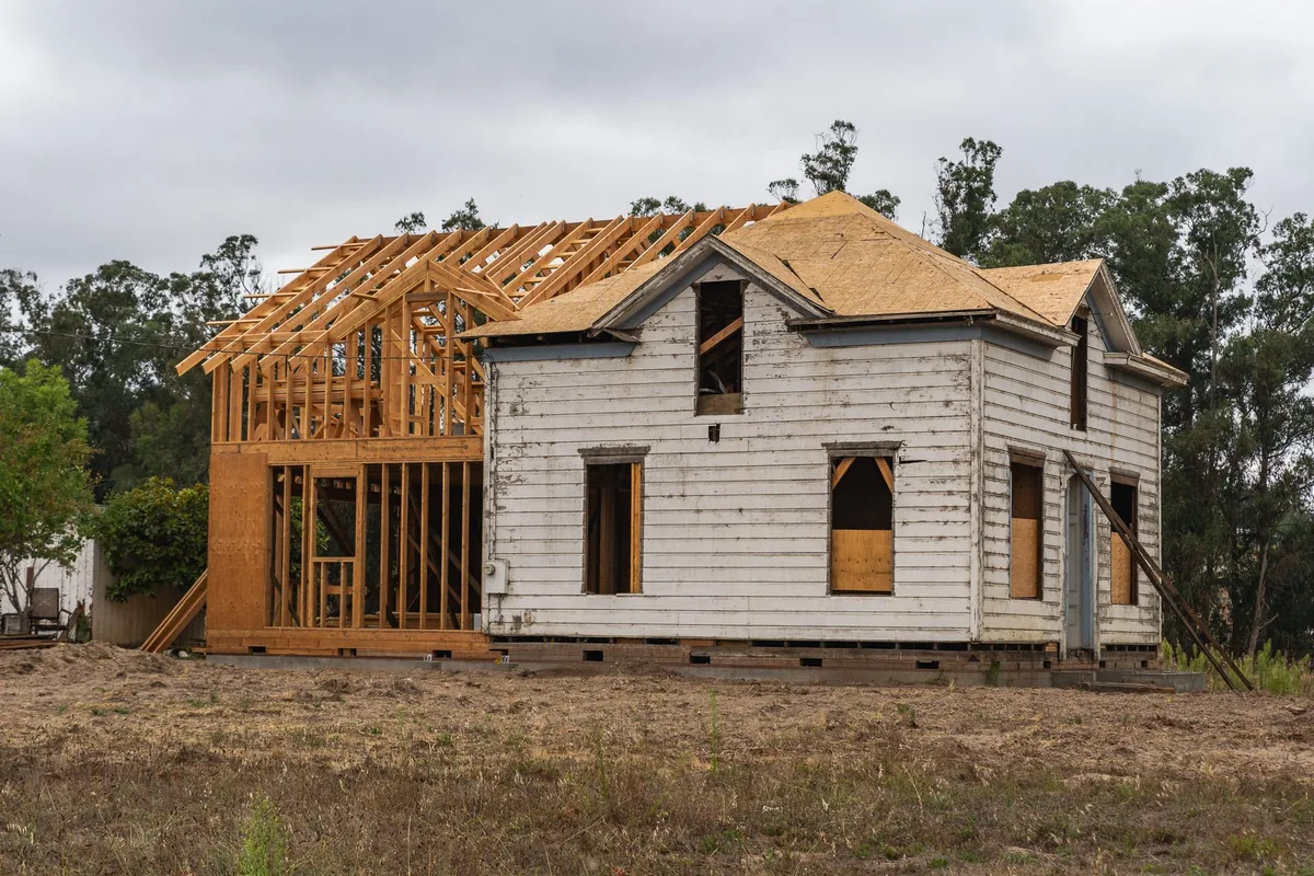 Older wooden house under renovation with new framing beside it