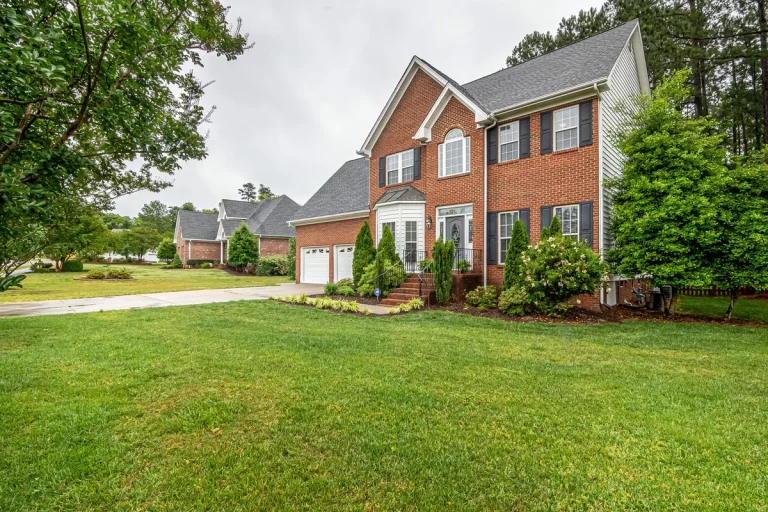 Two-story red brick house with a two-car garage and a landscaped front lawn.