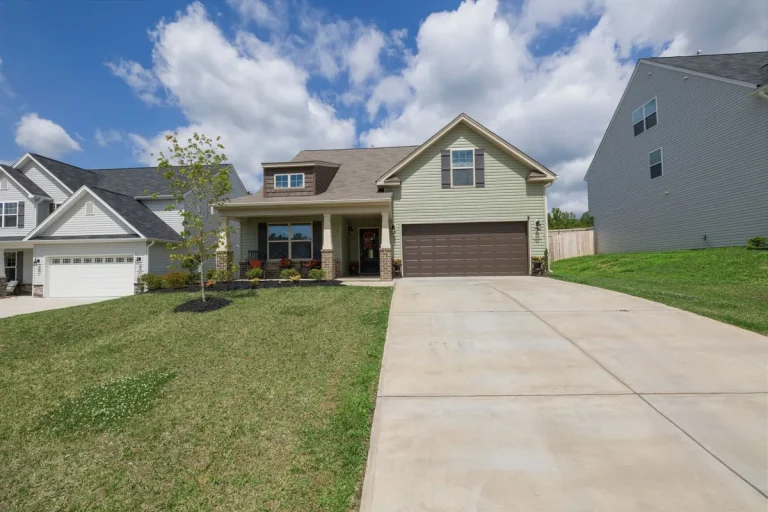 Two-story suburban house with a covered front porch and a concrete driveway under a partly cloudy sky.