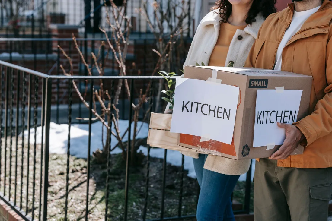 Two people carrying a moving box labeled kitchen